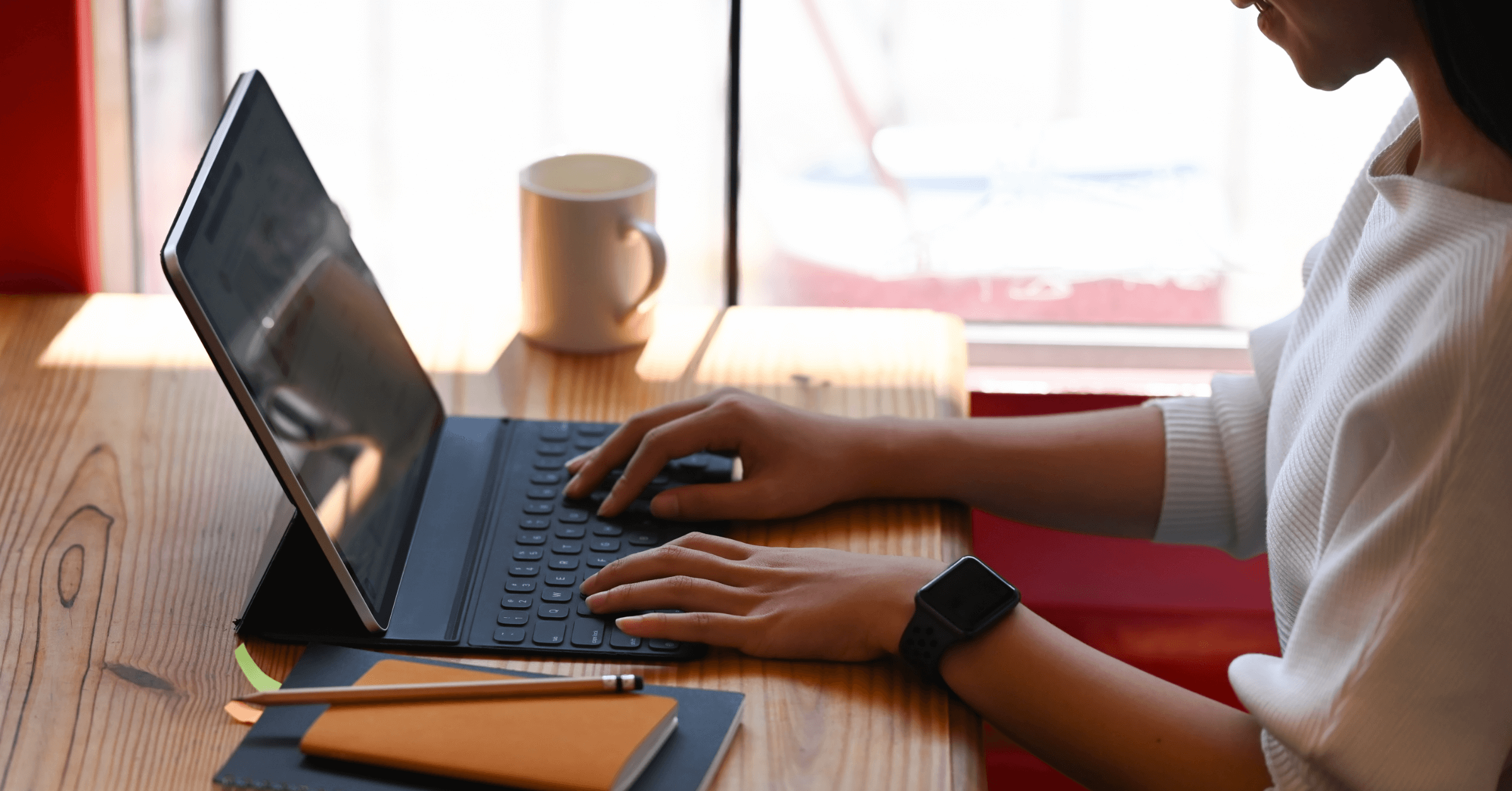 Kvinne jobber på laptop med notatblokken og kaffekoppen ved siden av