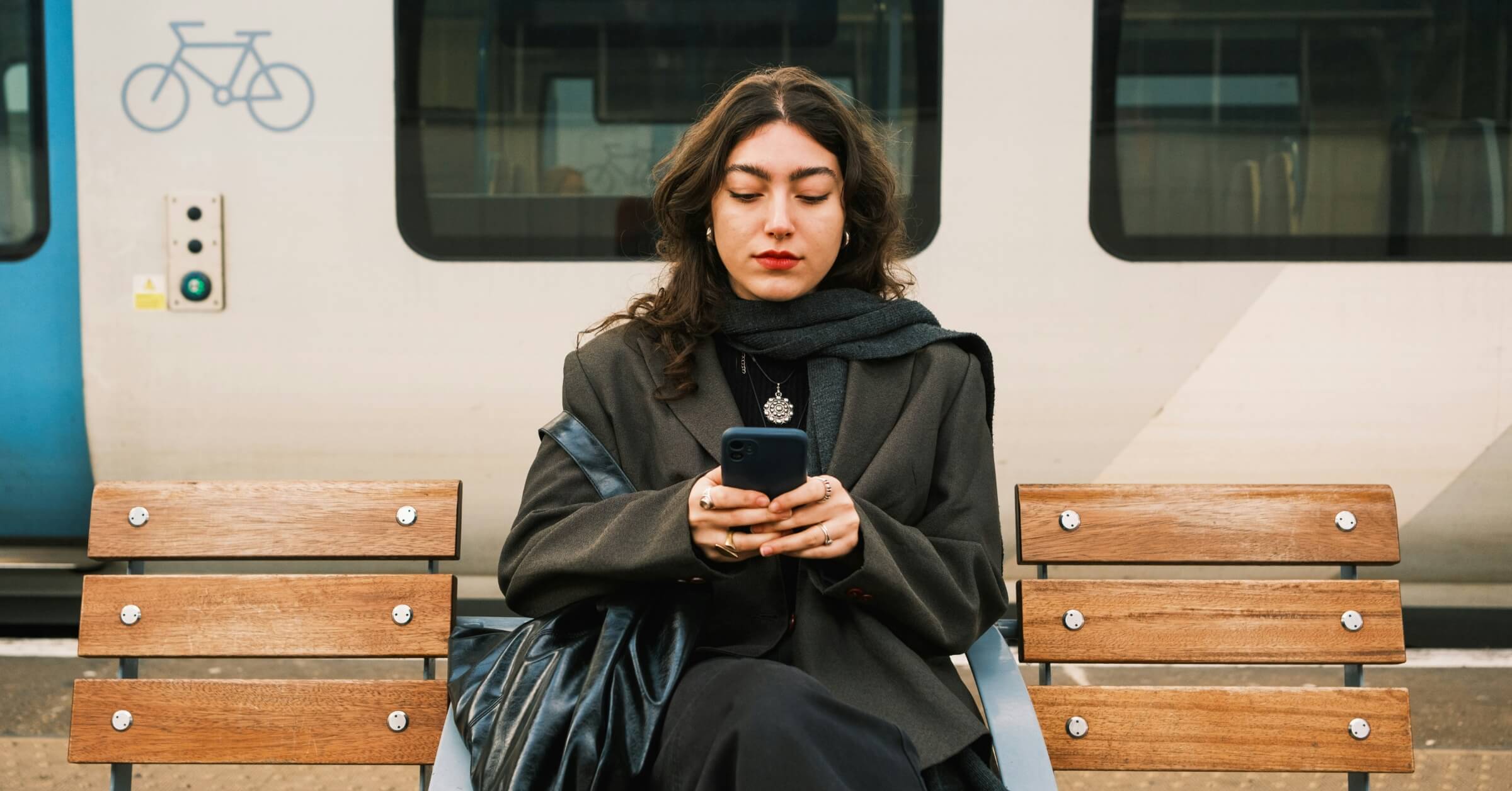 Kvinne sitter med mobilen på togstasjon