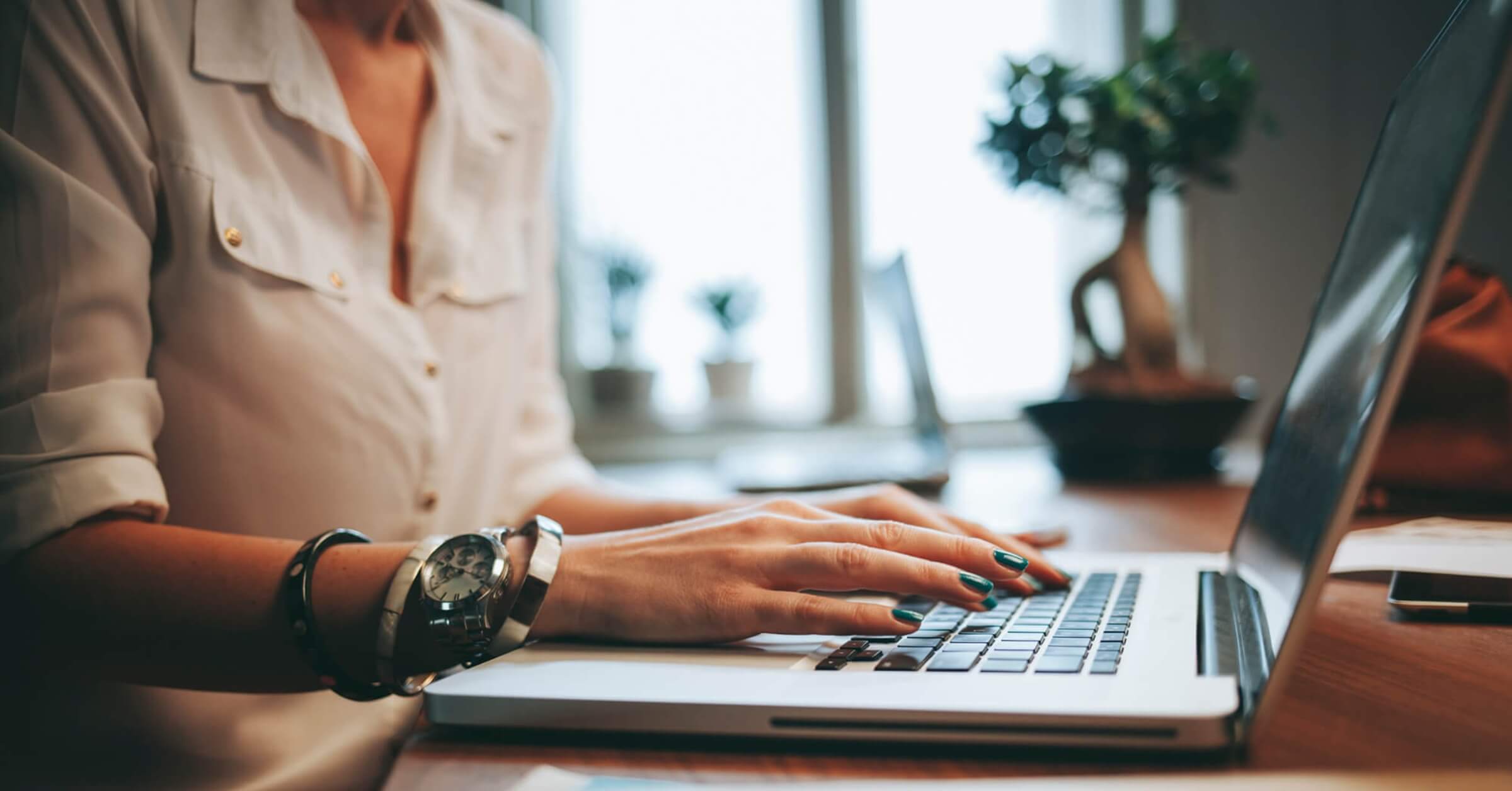 Kvinne med blå negler og klokke på håndleddet skriver på et en laptop