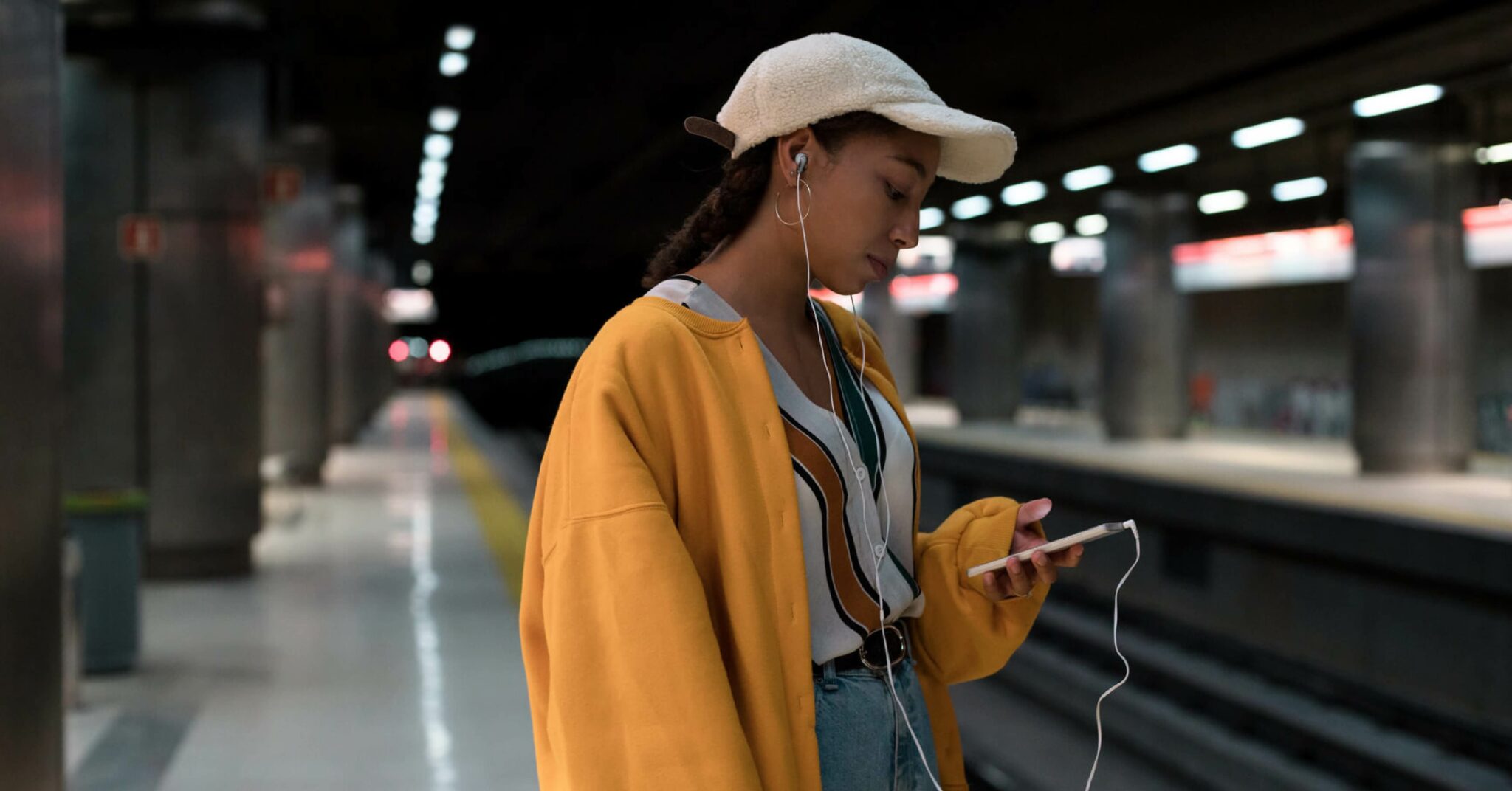 Ung kvinne med oransje jakke ser på mobilen mens hun venter på t-banen