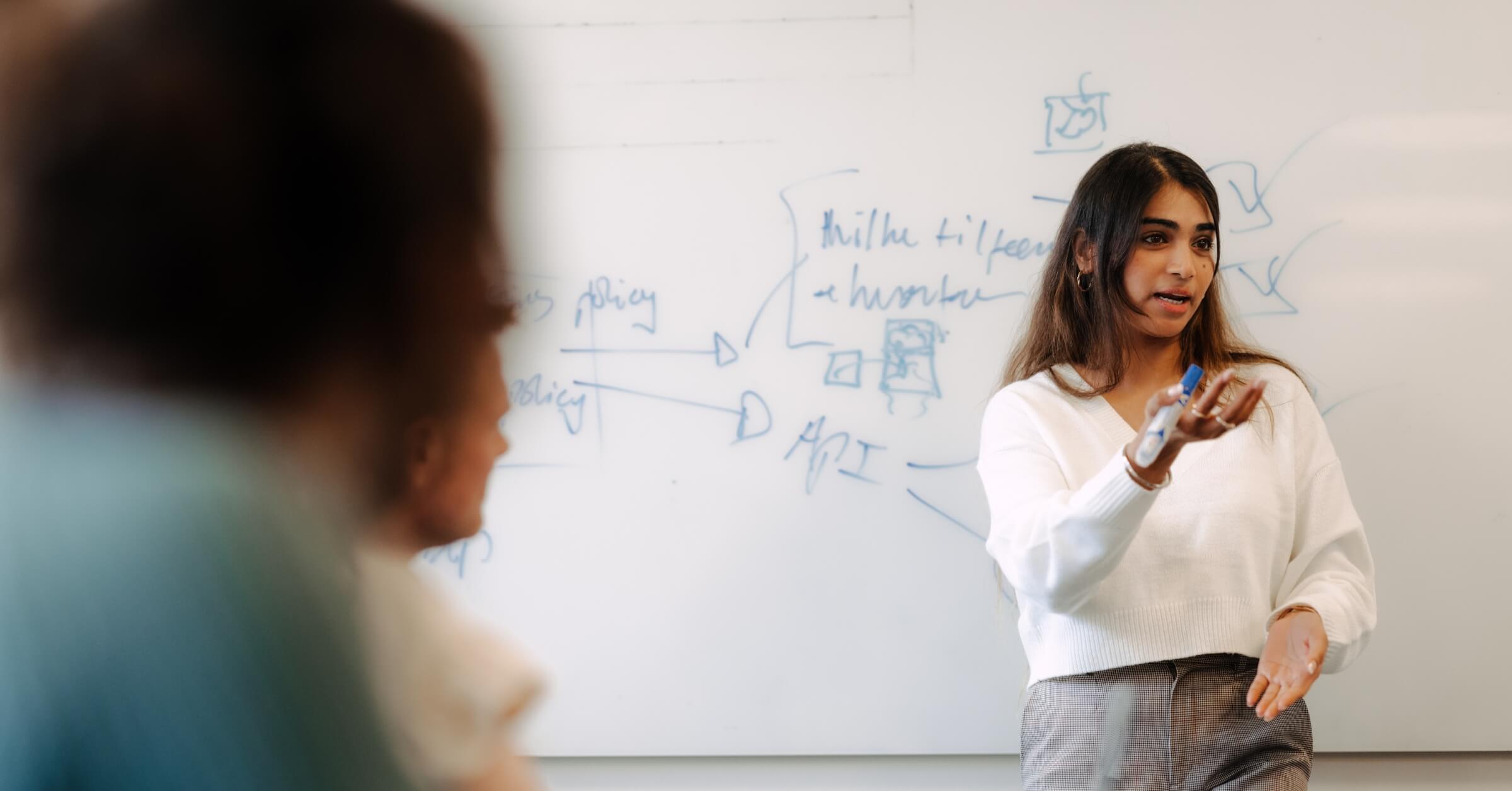 Kvinne presenterer foran kolleger på et whiteboard.